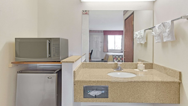 Un baño de hotel pequeño con microondas, refrigerador, lavamanos y perchero.
