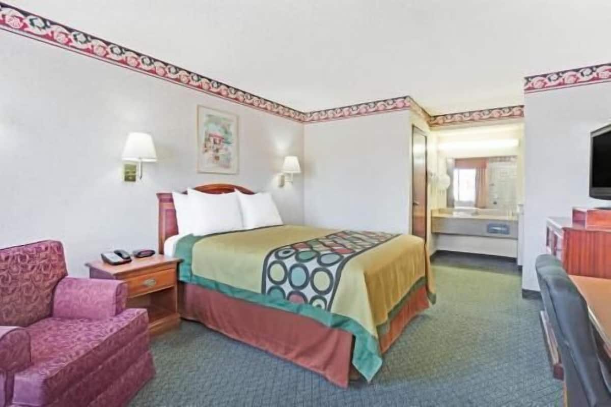 A hotel room with a bed, a chair, a desk, a television, and a bathroom visible through an open door.
