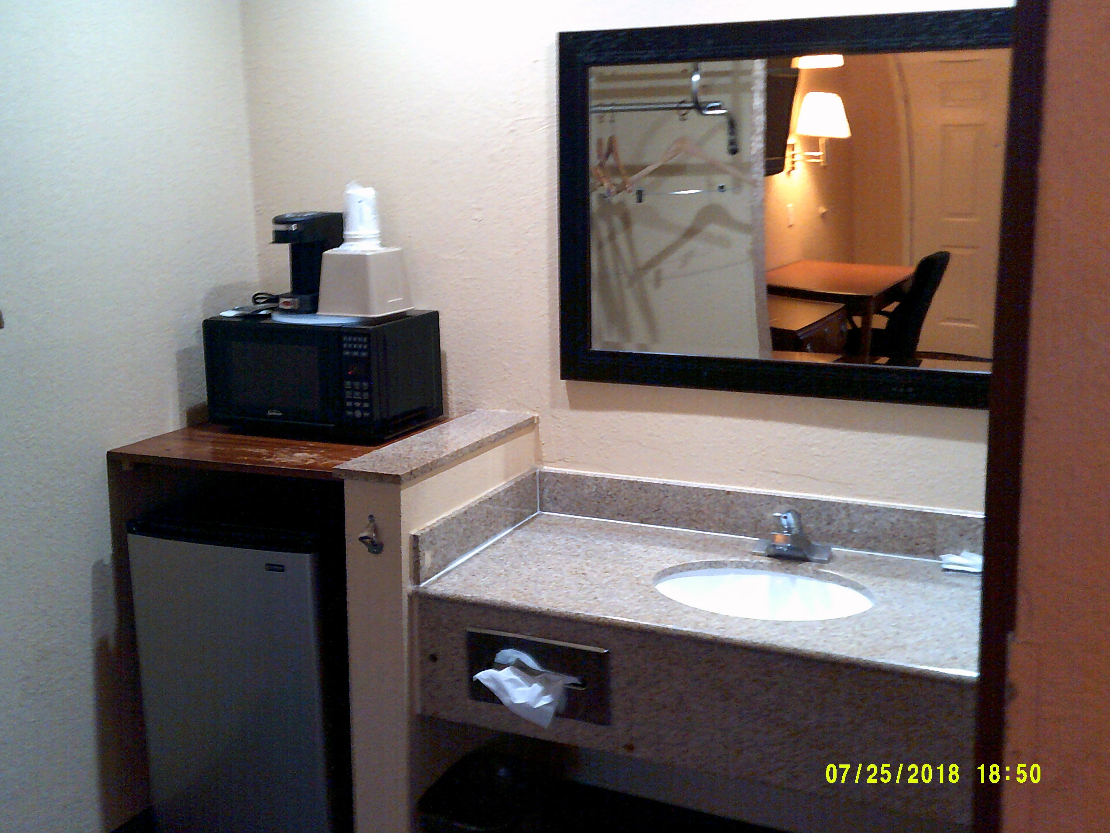 Un baño con lavamanos, espejo y microondas sobre un mueble pequeño.