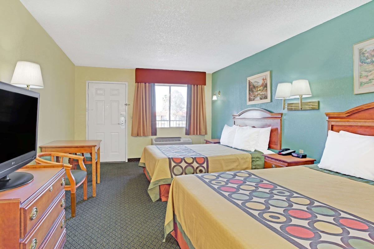 A hotel room with two beds, a TV, a dresser, and a window with curtains.