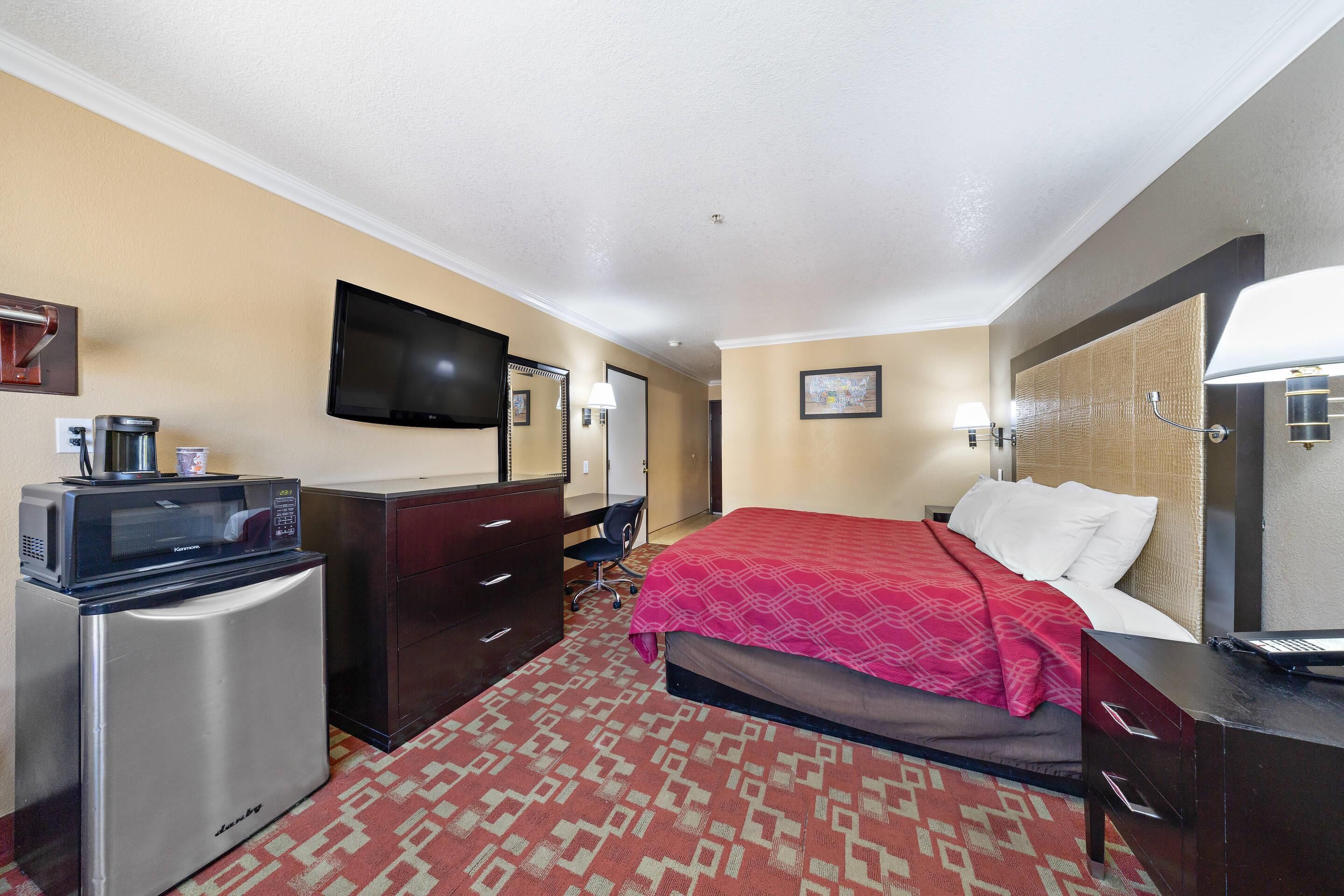A hotel room with a bed, a desk, a microwave, a television, and a dresser.