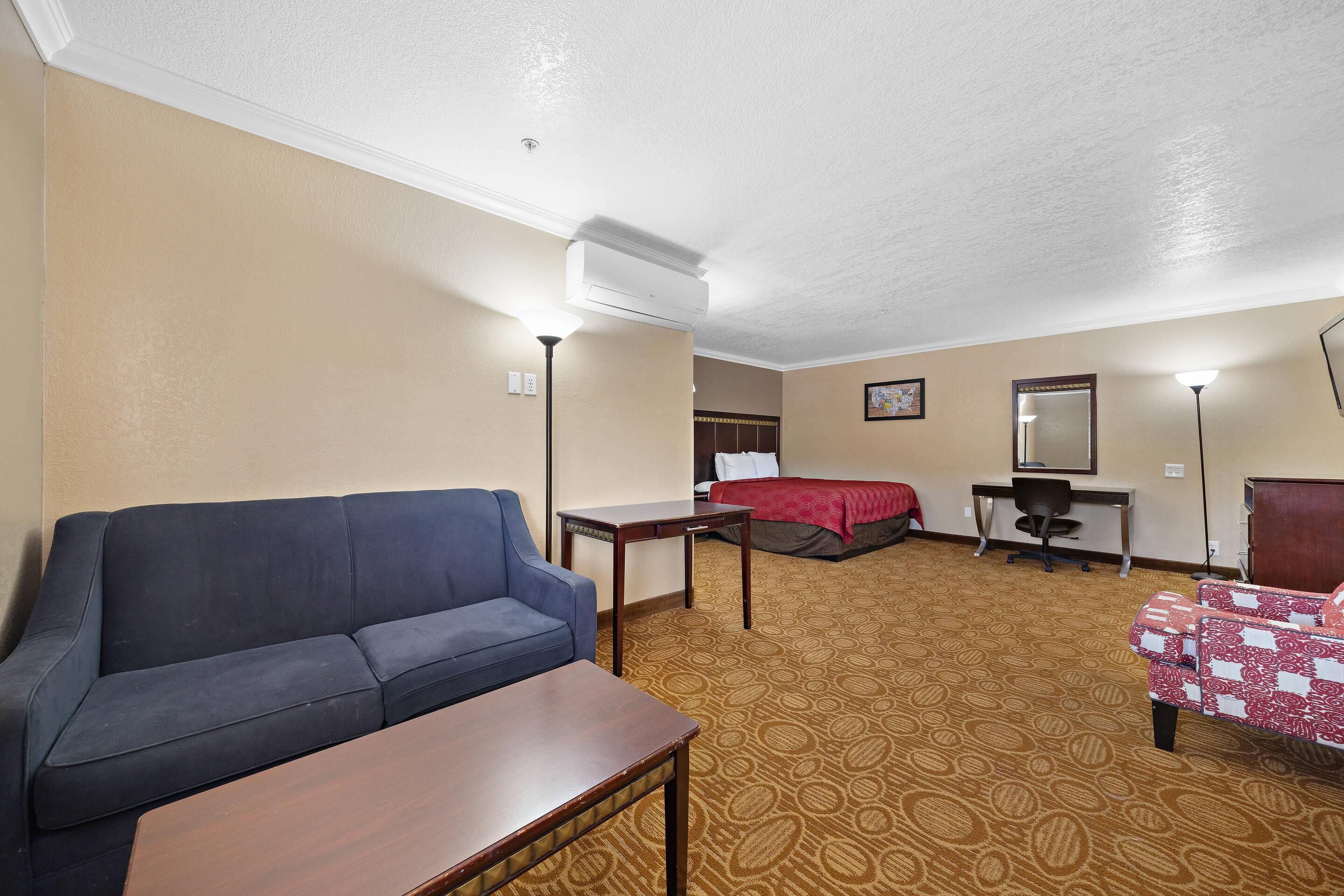 A hotel room with a sofa, a bed, a desk, a chair, and a table.