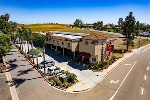 A hotel with a parking lot, a building with a red awning, and a grassy field in the background. - Econo Lodge Inn & Suites Fallbrook Downtown (Fallbrook)