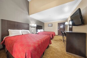 A hotel room with two beds, a desk, a television, and a patterned carpet.