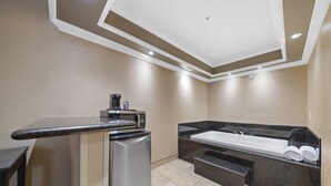 Une salle de bain d’hôtel compacte, équipée d’une machine à café intégrée, d’un petit réfrigérateur, d’une baignoire et d’un plan de toilette avec des serviettes.