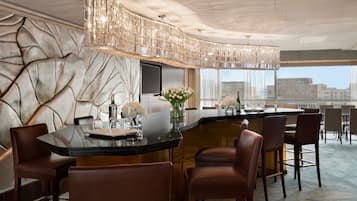 Un área de bar moderna con una barra curva, taburetes de cuero y un candelabro decorativo.