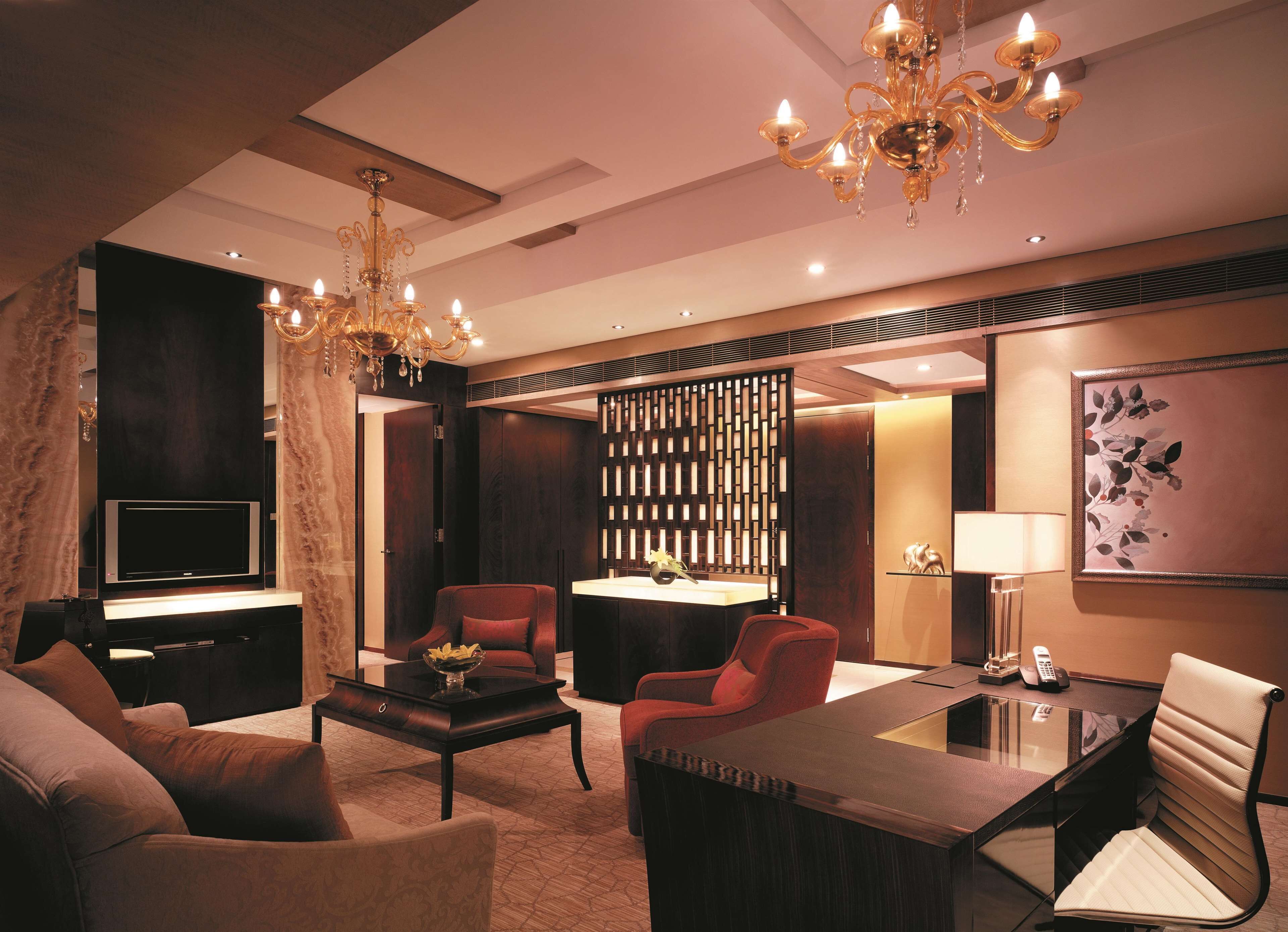 A modern living room with a TV, comfortable seating, a coffee table, and a decorative chandelier.