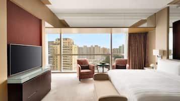 A hotel room with a large bed, a television, a seating area, and a view of the cityscape.