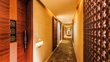 Un pasillo de hotel con puertas de madera, alfombra estampada y un detalle decorativo en la pared.