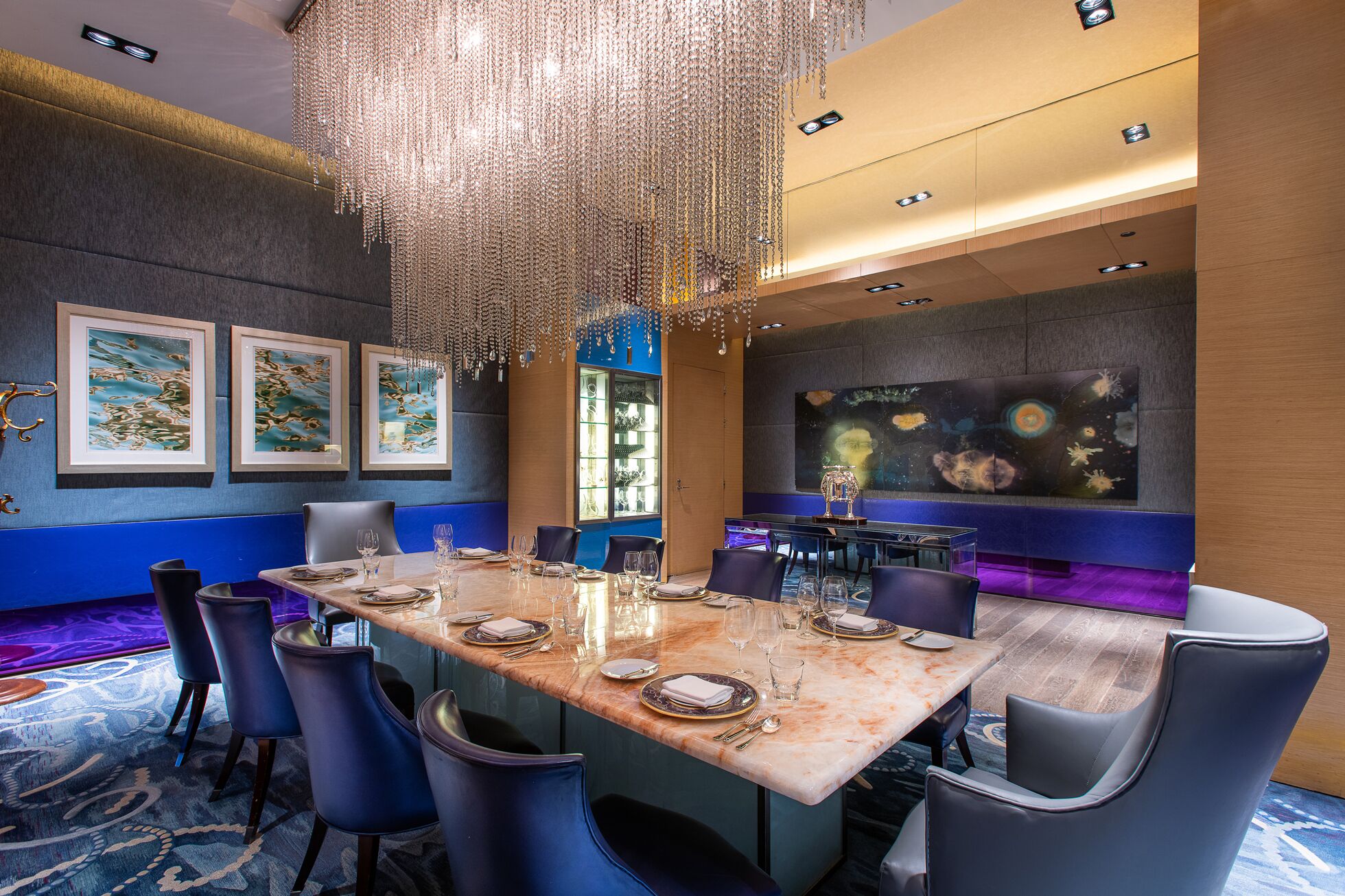 A dining area with a marble table, blue chairs, and a chandelier.