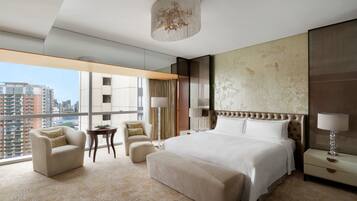 Une chambre d’hôtel moderne dotée d’un grand lit, d’un coin salon avec un fauteuil et un pouf, d’une petite table et d’une grande fenêtre donnant sur la ville.
