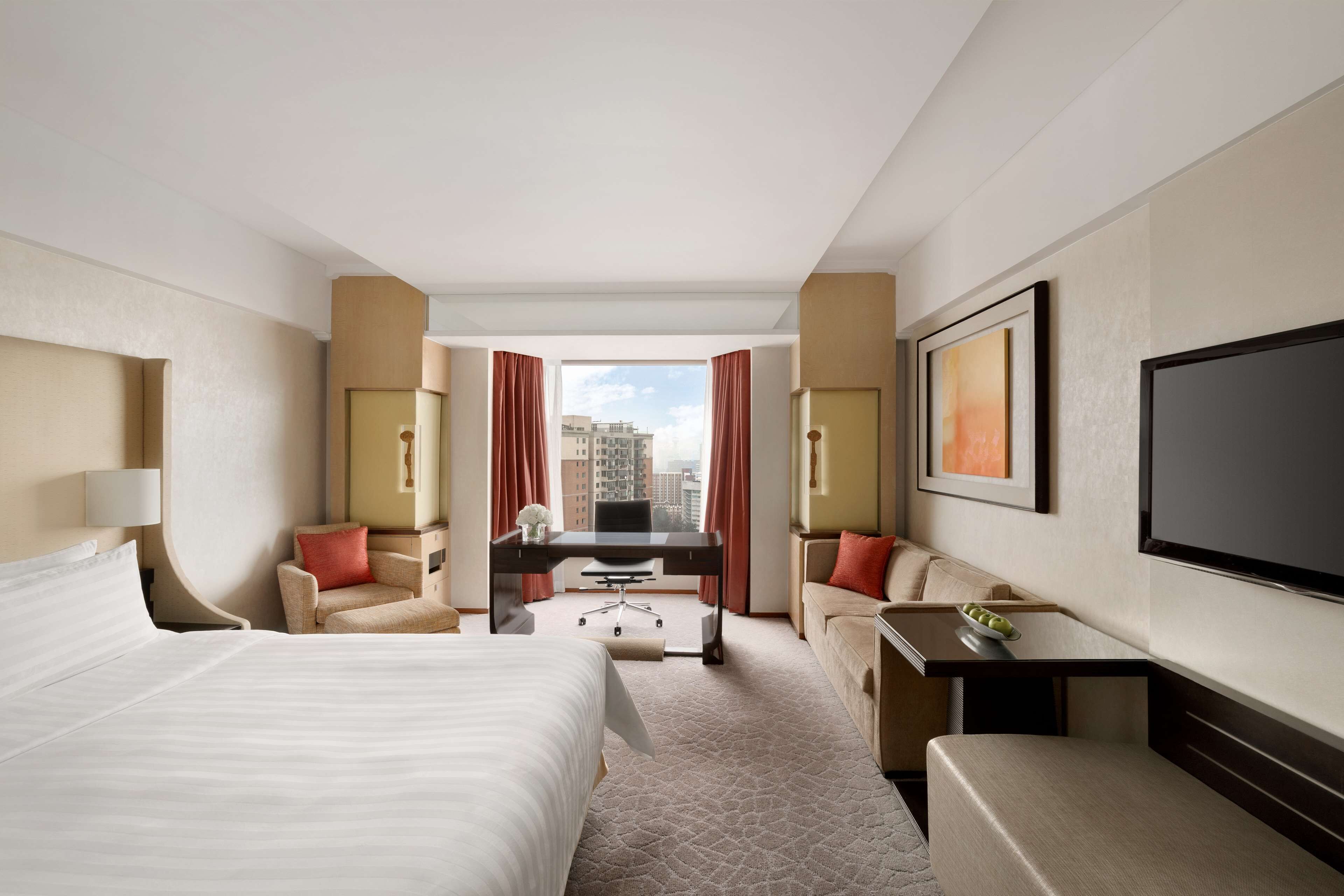 A hotel room with a large bed, a desk, a sofa, and a TV.