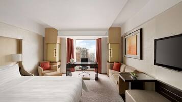 A hotel room with a large bed, a desk, a sofa, and a TV.