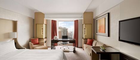 A hotel room with a large bed, a desk, a sofa, and a TV.