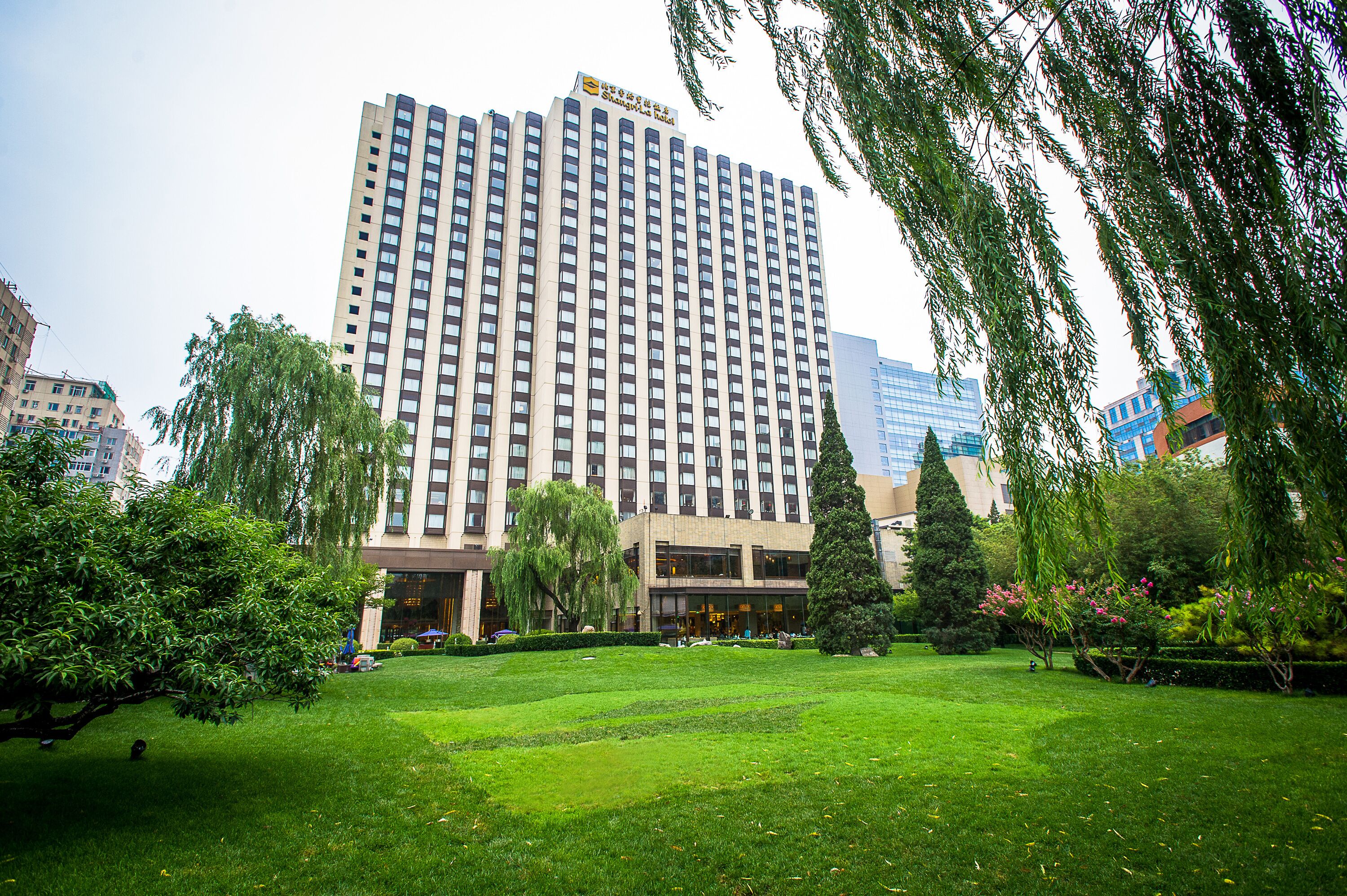 A tall hotel with a modern facade, surrounded by a well-maintained grassy area and trees.