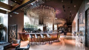 A modern bar area with a curved bar, multiple seating options, and a unique ceiling light fixture. - Shangri-La Beijing (Beijing)