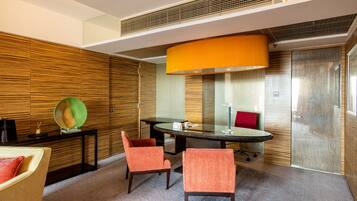 Une salle de conférence moderne avec une table en verre, deux chaises orange, un coussin rouge et un grand luminaire suspendu orange.