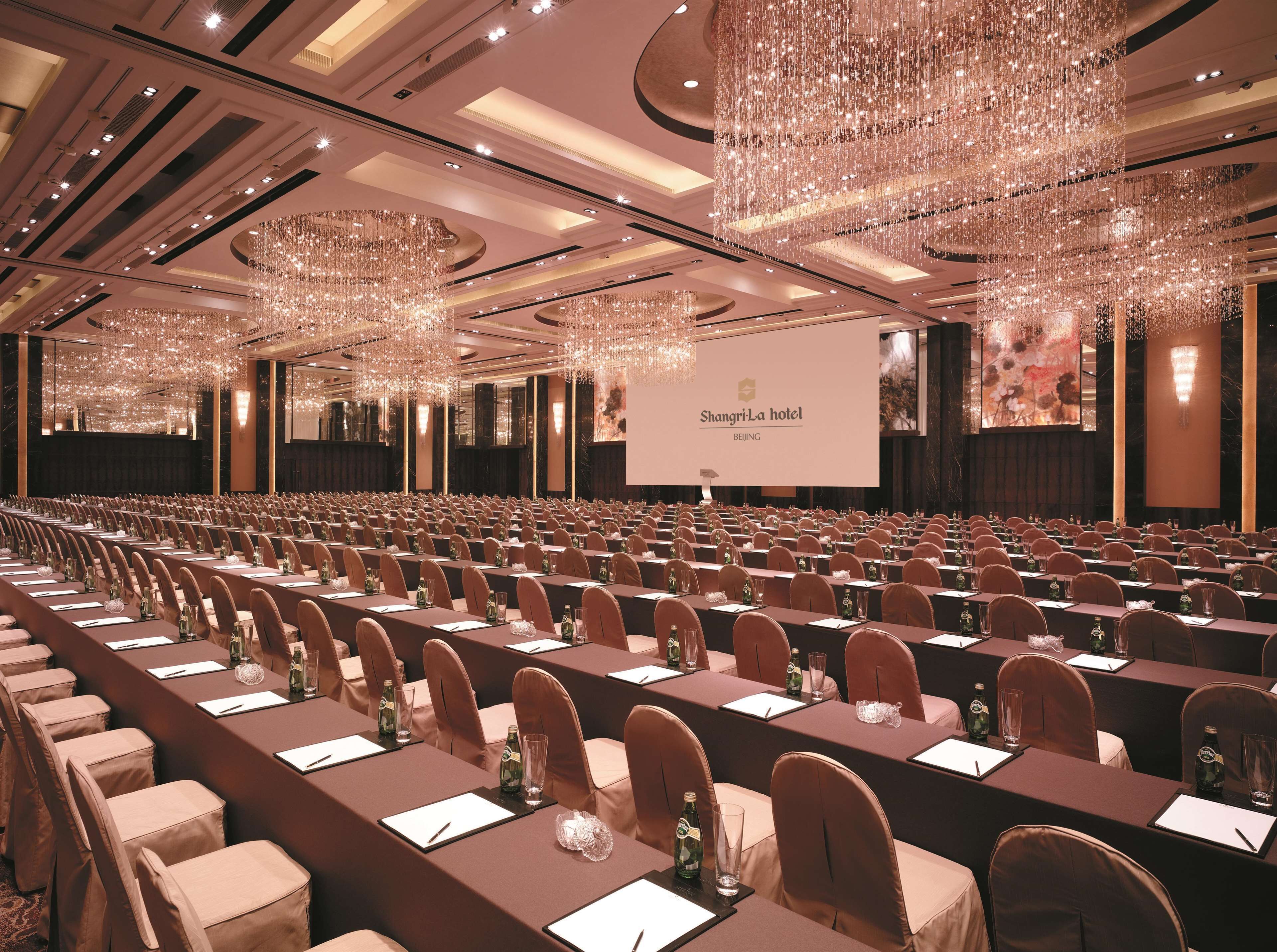 Une salle de conférence à l’hôtel Shangri-La de Pékin, avec des rangées de tables, de chaises et un grand écran.