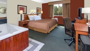 A hotel room with a large bed, a desk with a computer, a chair, a TV, a bathroom with a bathtub, and a window with curtains. - Travelodge by Wyndham Jackson (Jackson)