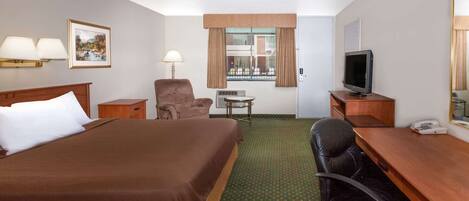 A hotel room with a large bed, a desk with a computer, a chair, a TV, and a window with curtains.