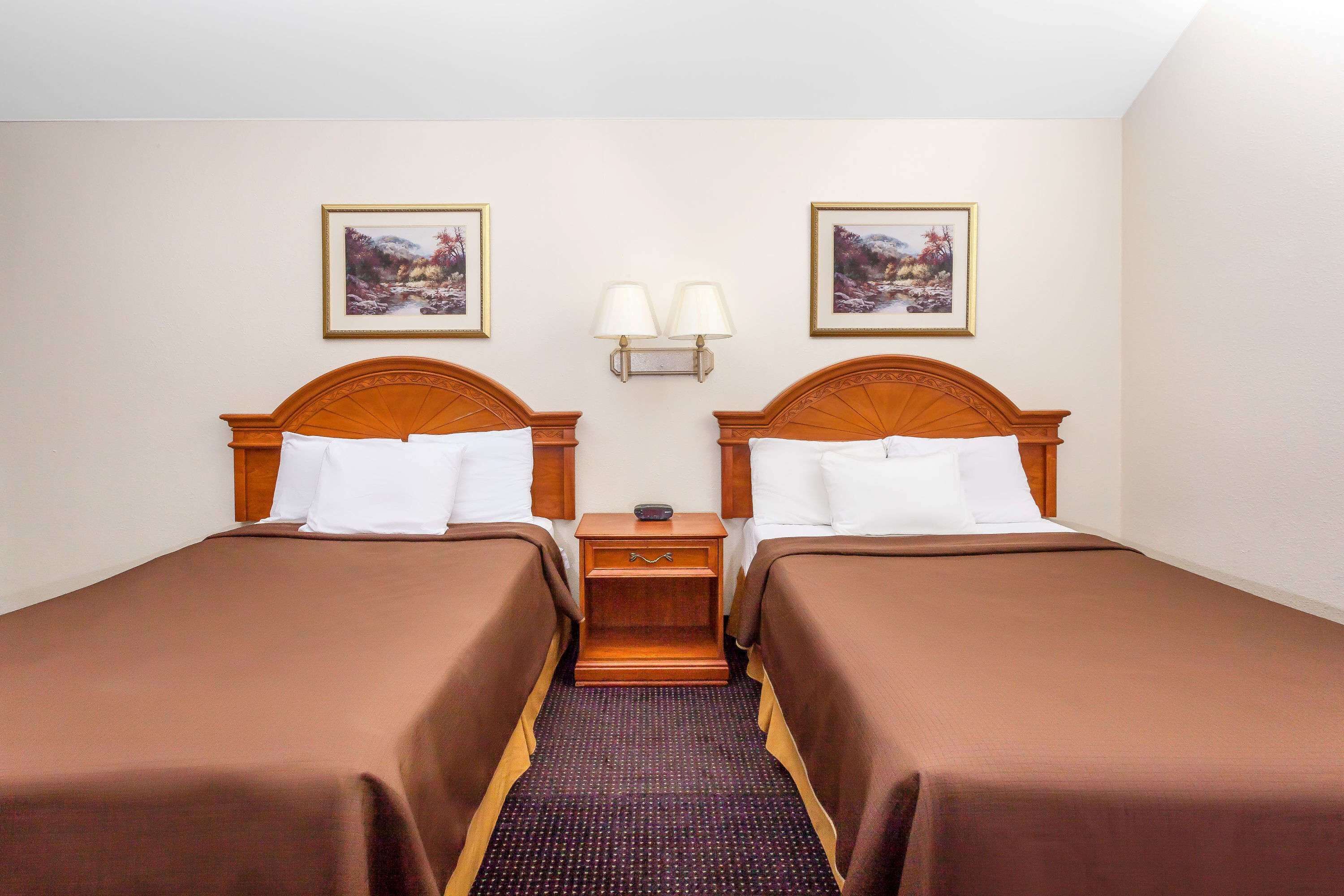 A hotel room with two single beds, a nightstand with lamps, and two framed pictures on the wall.