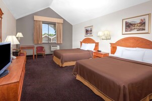 Habitación de hotel con dos camas, un escritorio con televisor, una silla, una ventana con cortinas y dos lámparas de pared.