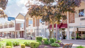 A Travelodge hotel with a brick facade, a covered outdoor seating area, and a landscaped garden with benches. - Travelodge by Wyndham Jackson (Jackson)