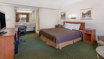Habitación de hotel con cama, escritorio, silla, televisor, baño y dos cuadros en la pared.
