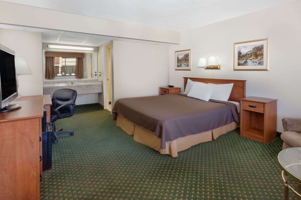 Habitación de hotel con cama, escritorio, silla, televisor, baño y dos cuadros en la pared.