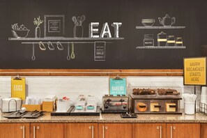 A breakfast buffet area with a chalkboard displaying the word "EAT" and various food items.