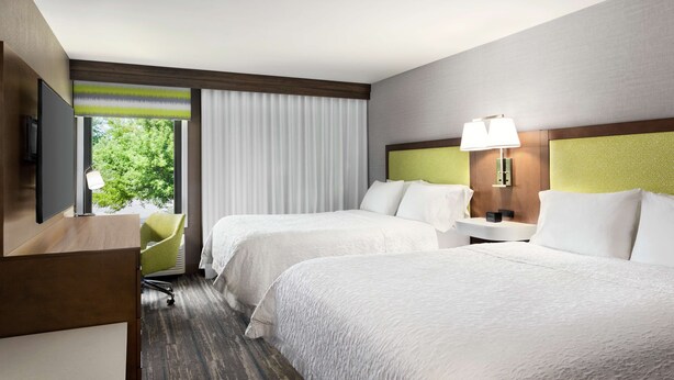 Une chambre d’hôtel avec deux lits, un bureau avec une chaise, une télévision et une fenêtre avec des rideaux.