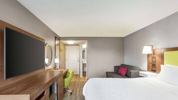 Habitación de hotel con cama, escritorio con televisor de pantalla plana, silla verde, sofá y puerta que da a un baño.