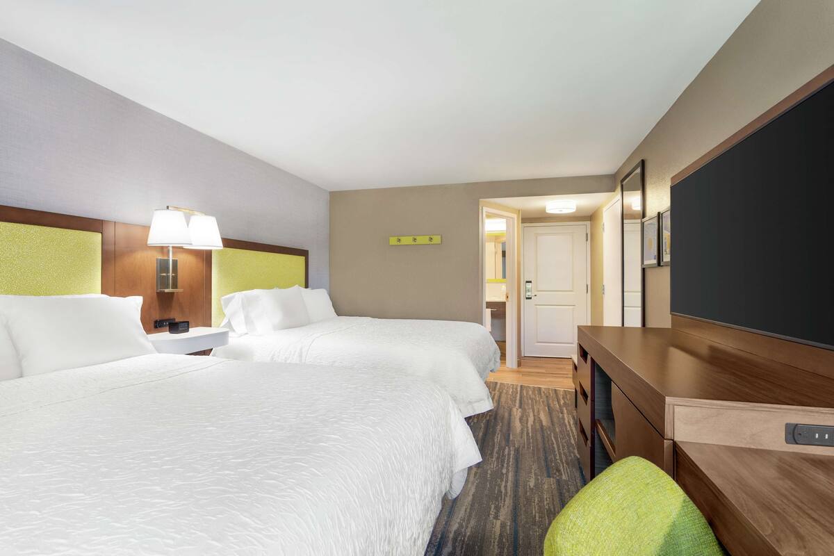 A hotel room with two beds, a desk, a lamp, and a television.