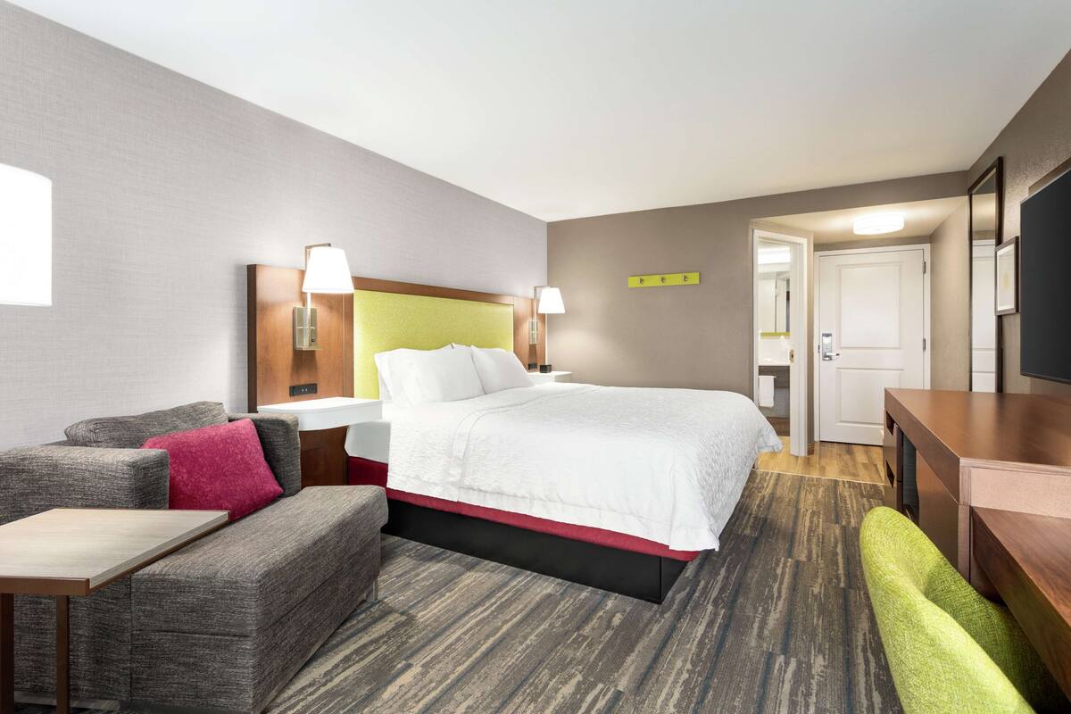 A hotel room with a bed, a sofa, a desk, and a television.