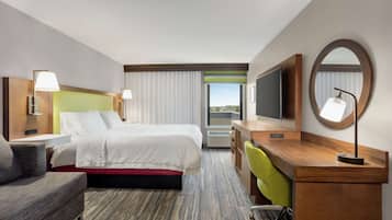 A hotel room with a bed, a desk, a chair, a TV, and a large window with a view.