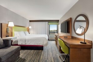 A hotel room with a bed, a desk, a chair, a TV, and a large window with a view.