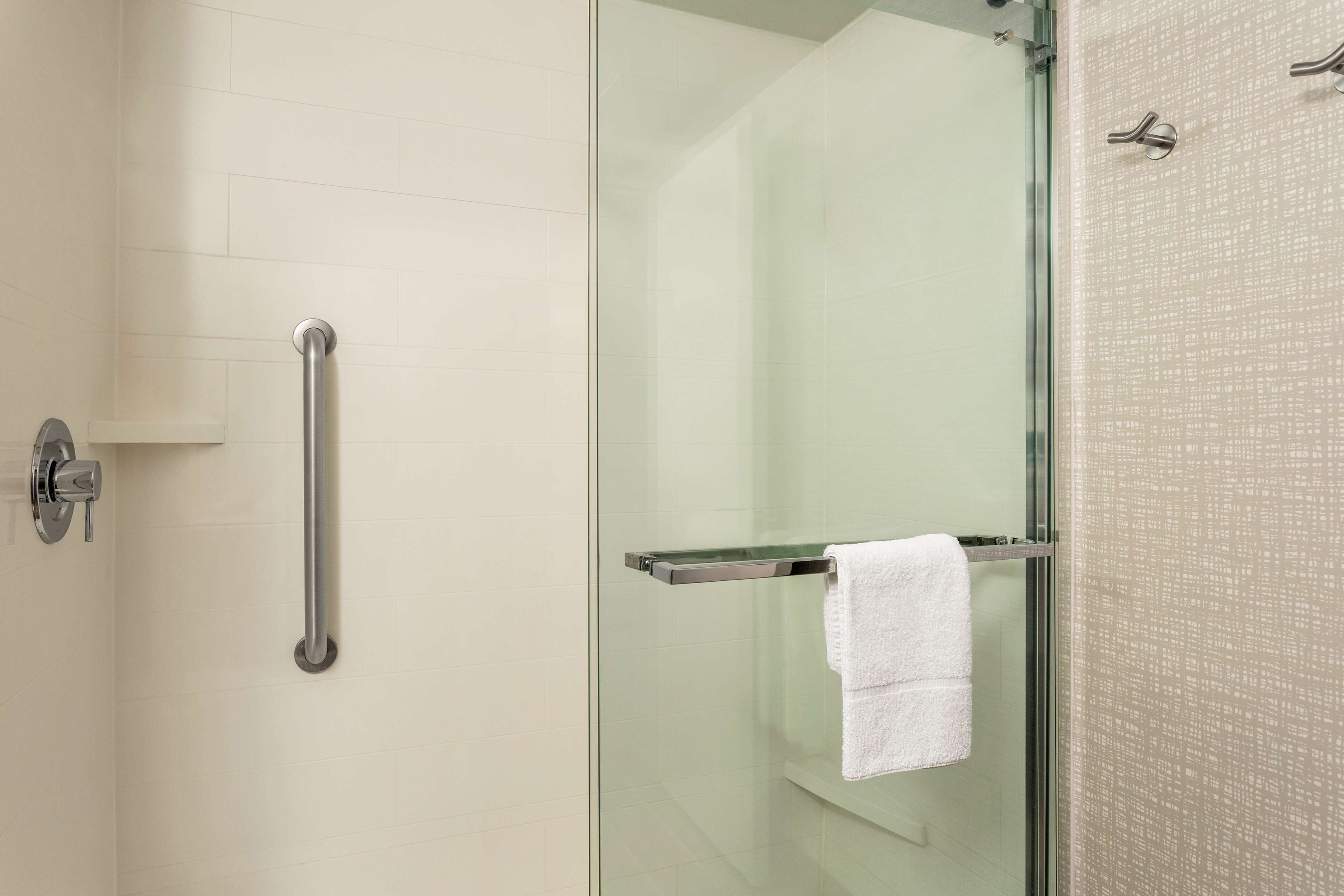 A glass-enclosed shower area with a glass door, a white towel hanging on a metal towel bar, and a handrail on the left.