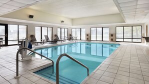 Une piscine intérieure avec des parois en verre transparent, un sol carrelé et des échelles métalliques.