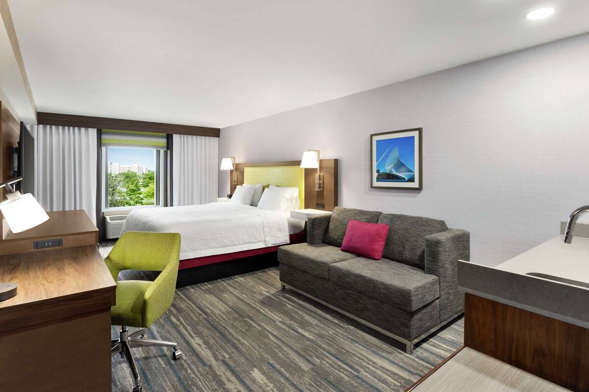 A hotel room with a bed, a sofa, a desk, and a bathroom.