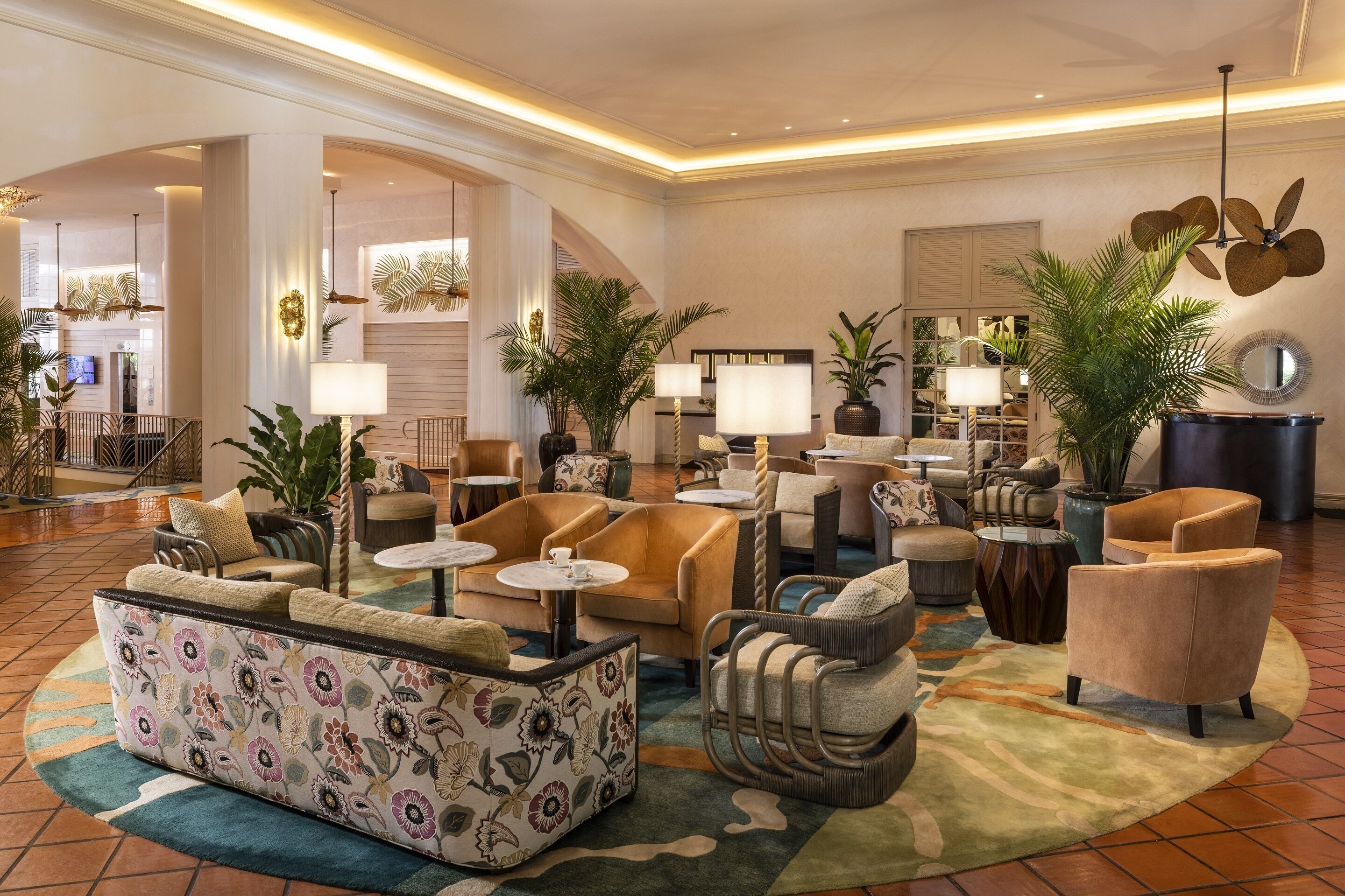 A spacious lobby with a variety of seating options, including sofas, armchairs, and a patterned sofa. There are multiple tables and a large mirror.