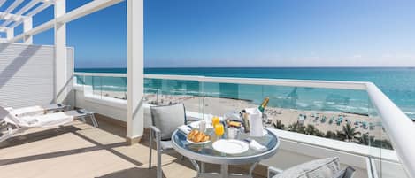 A balcony with a table set for breakfast, overlooking a beach.