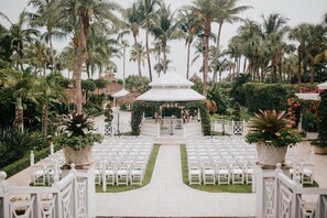 A wedding ceremony setup with white chairs and a central aisle leading to a gazebo.