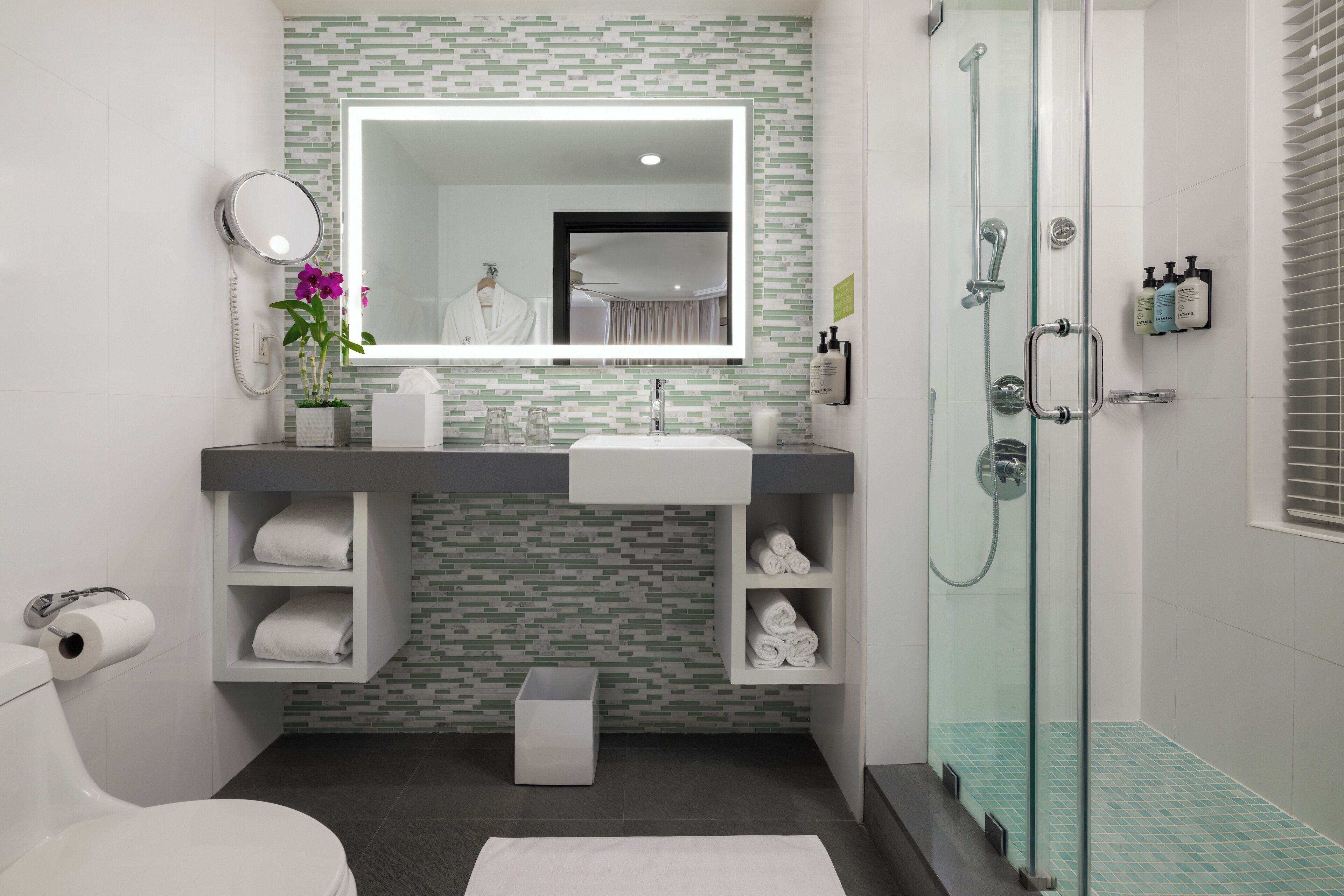 A modern bathroom with a glass-enclosed shower, a large mirror, and a white sink.