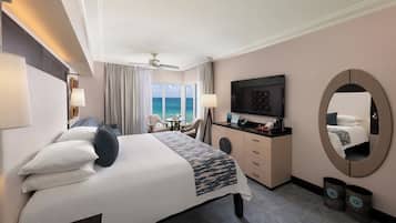 Een hotelkamer met een bed, bureau, televisie, plafondventilator en uitzicht op zee.