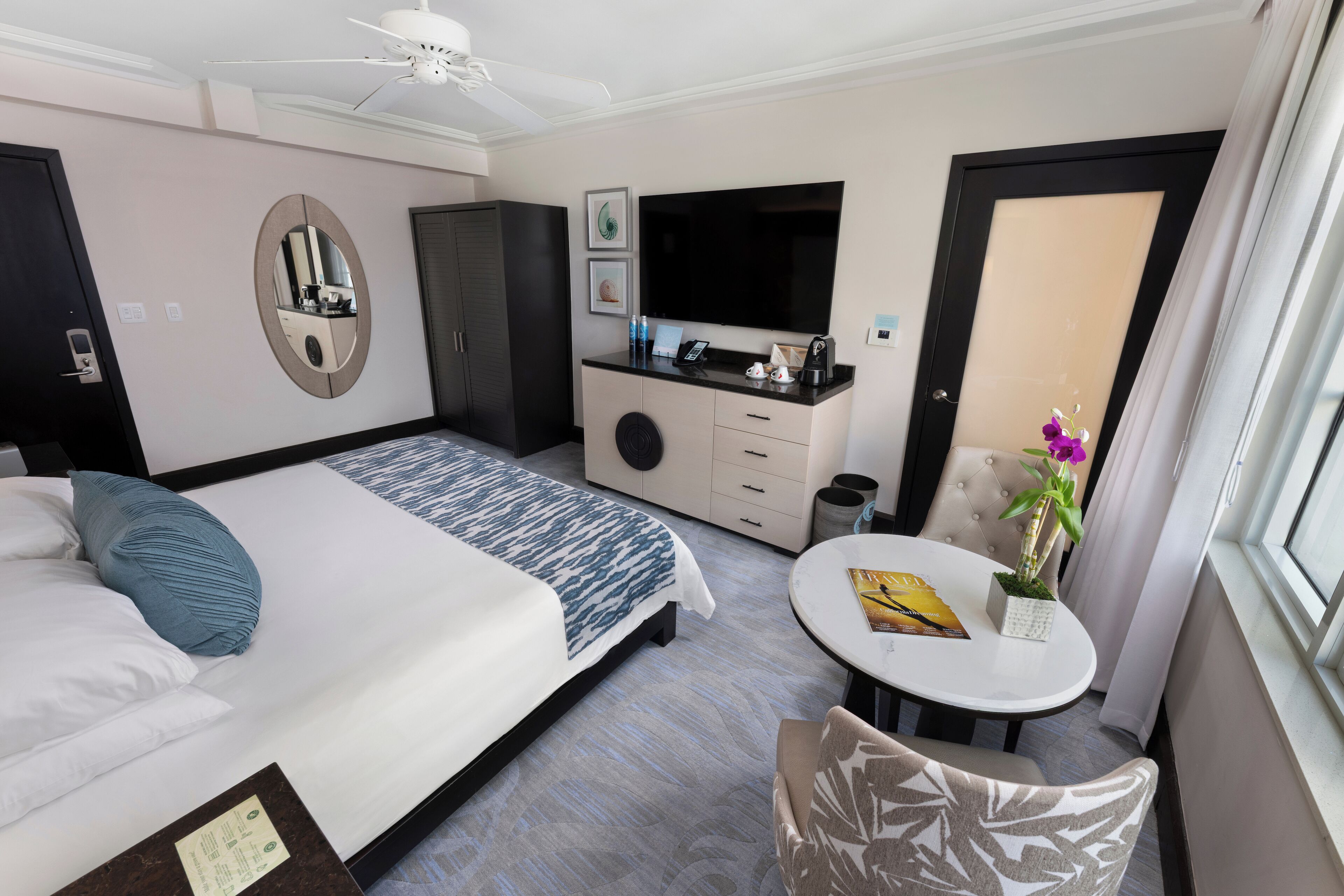 A hotel room with a bed, a desk, a TV, a mirror, and a window.