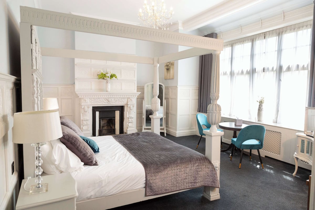 A four-poster bed with a fireplace, a chandelier, and a view of the city through large windows.