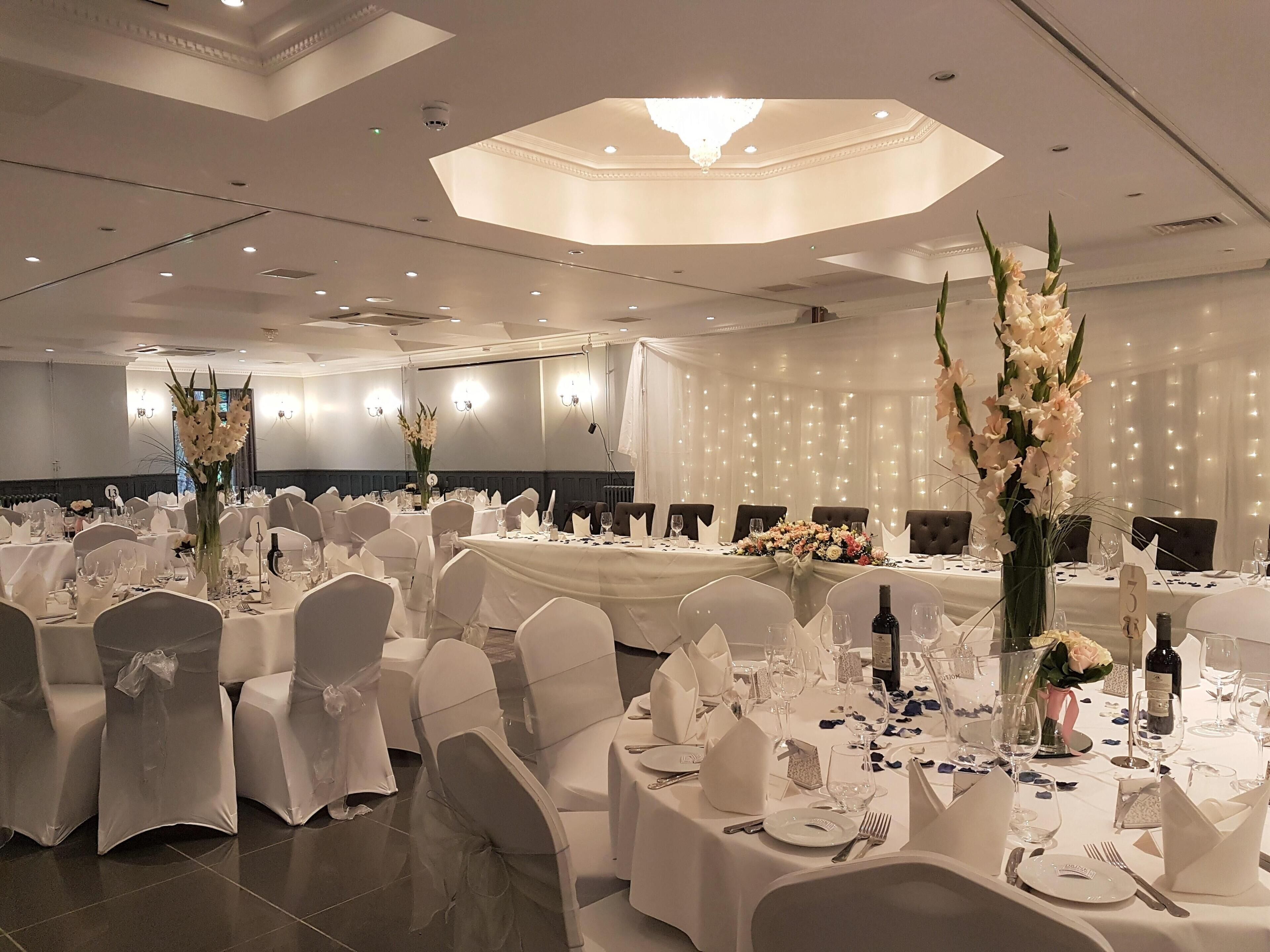Un salón de banquetes con mesas redondas, manteles blancos y sillas cubiertas con tela blanca.