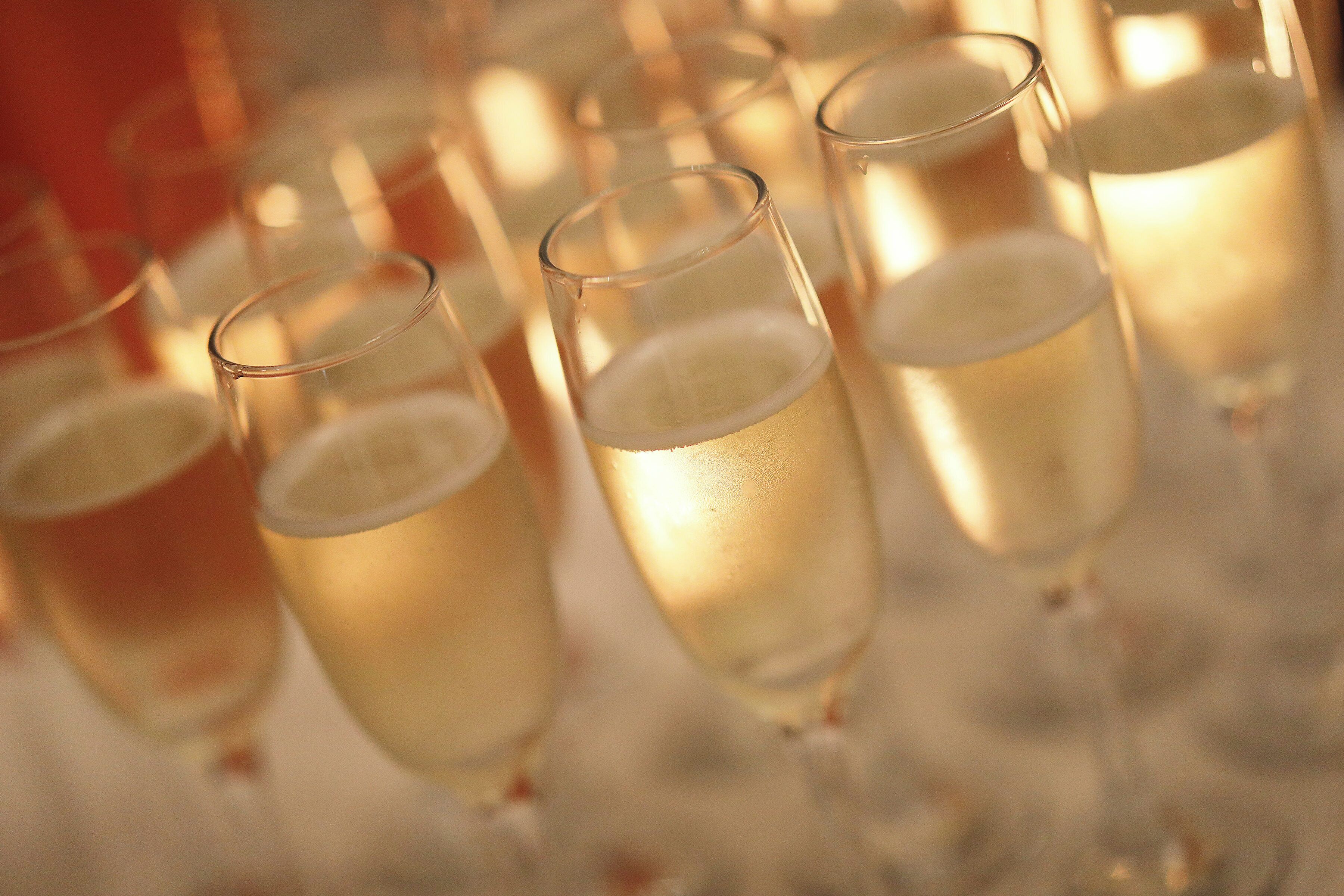 A row of champagne glasses filled with a light-colored beverage, likely champagne, on a reflective surface.
