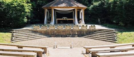 A gazebo with a tiled roof and white drapes, surrounded by a gravel area with benches.