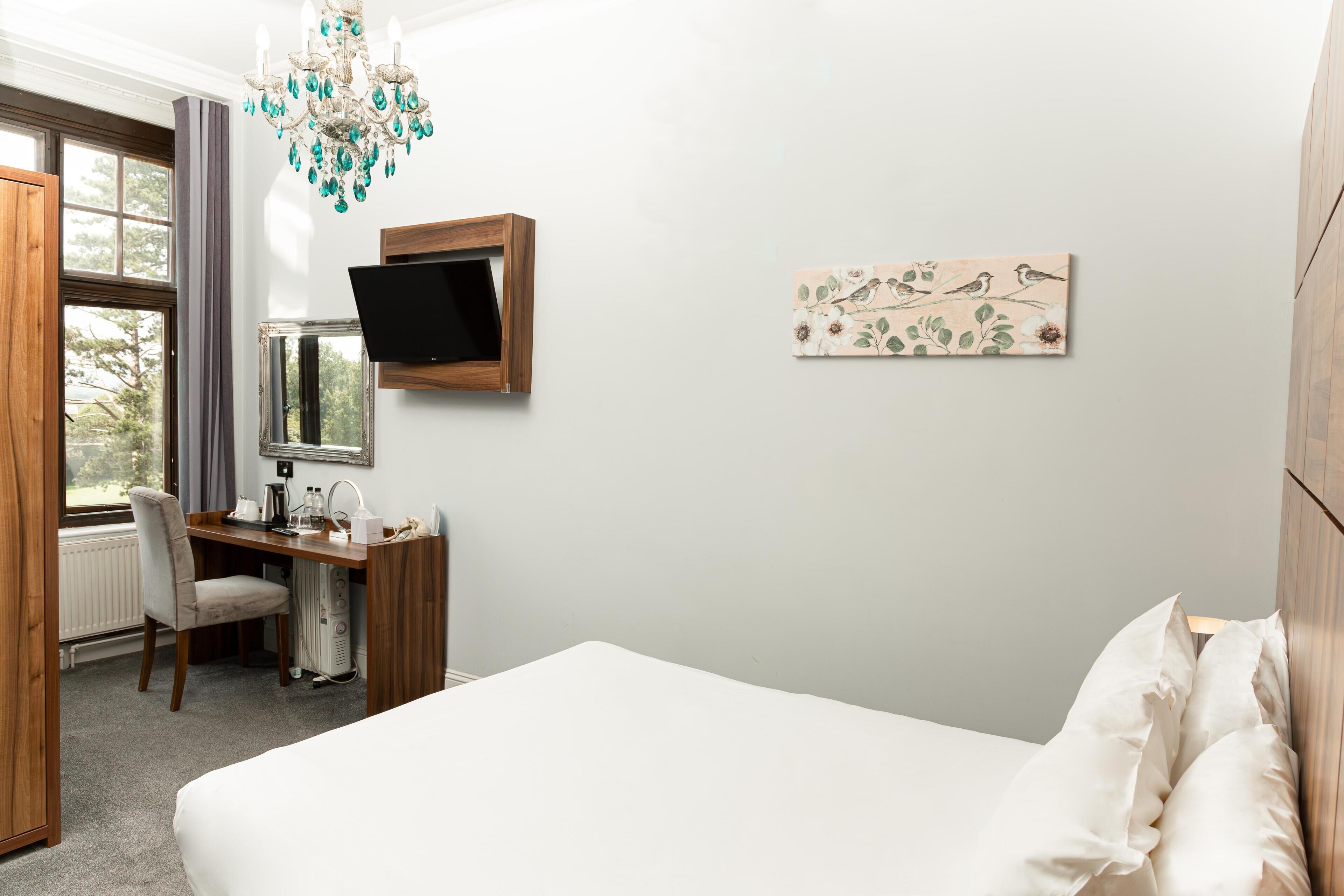 A hotel room with a bed, desk, chair, TV, and artwork on the wall.